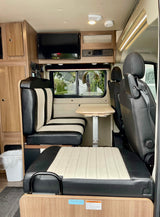 RV rental's inviting interior shows comfortable black & cream dinette, table, and entertainment unit.