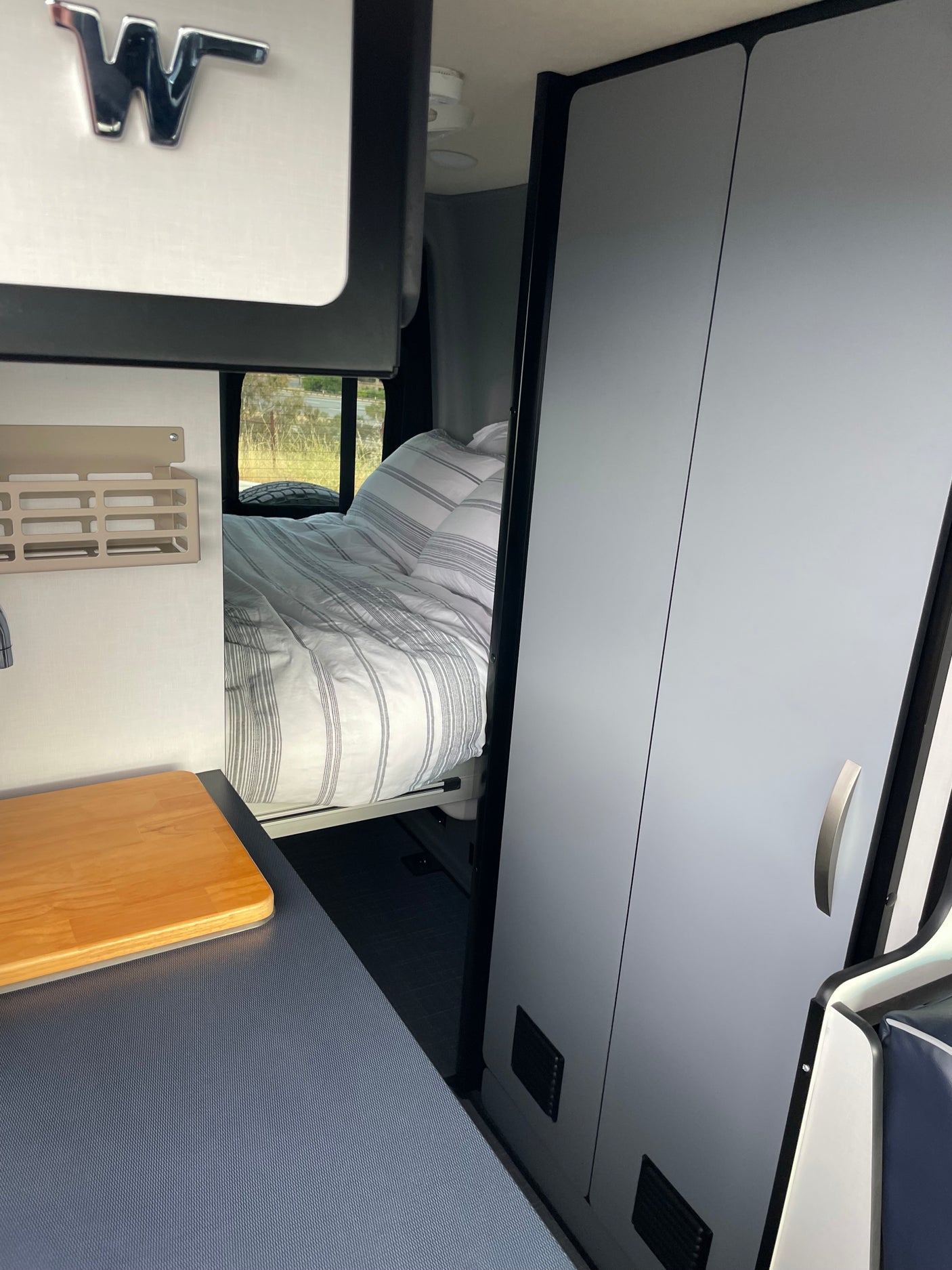 Winnebago rv rental interior: a comfy bed, kitchenette with wood counter, and sleek storage cabinets.