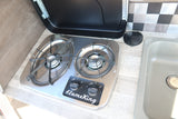 RV rental kitchen with stainless steel FlameKing two-burner stovetop and light gray sink, with an open lid.