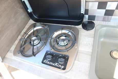 RV rental kitchen with stainless steel FlameKing two-burner stovetop and light gray sink, with an open lid.
