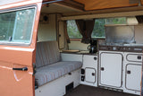 Inside a retro Westfalia camper van, great for an RV rental. Features a striped bench, compact kitchen with stove, and storage.