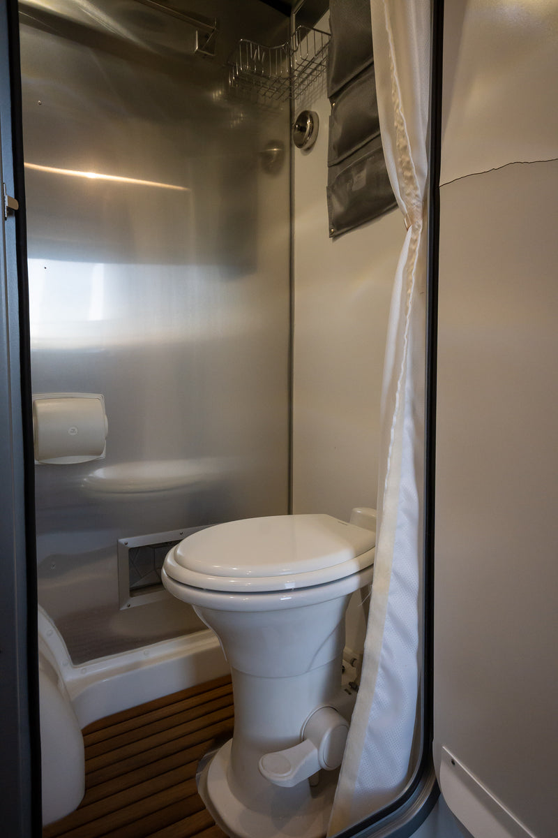 Compact RV rental wet bath featuring a toilet, shower area with metallic walls, and a slatted wooden floor. — photo 20