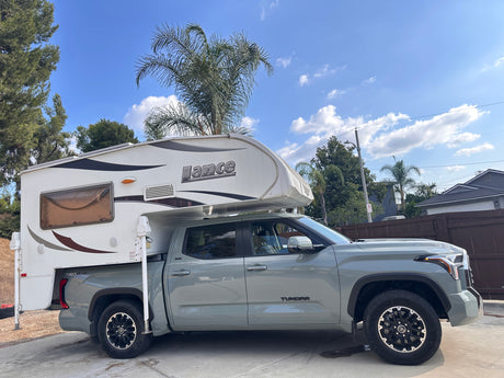 Light grey Toyota Tundra pickup with a white Lance truck camper, ideal for an RV rental adventure.