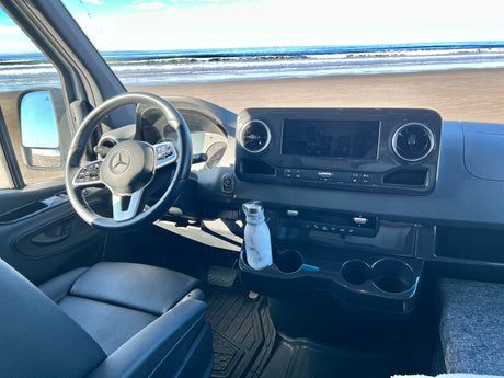 Panoramic beach view from a modern RV rental dashboard, featuring the steering wheel, controls, and infotainment screen.