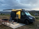 rv rental camper van: illuminated interior, extended awning, picnic table, and dog enjoying a peaceful campsite evening.