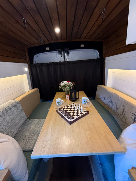 Enjoy your rv rental! This cozy camper van interior features a wooden ceiling, dining table, chessboard, and comfy benches.
