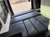 Modern rv rental: a versatile gray leatherette bed/seating area, outdoor window view, and integrated kitchen counter visible.