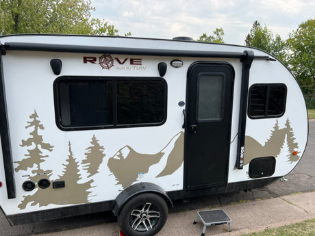 Compact white Rove travel trailer with black accents and a scenic mountain/tree decal, ready for your next RV rental adventure.