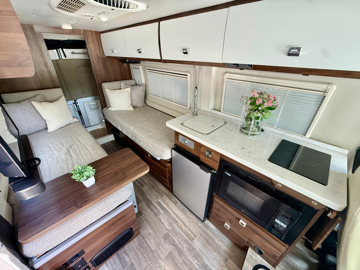 Modern rv rental interior featuring a kitchen with microwave, fridge, and cozy seating/sleeping areas. — photo 10
