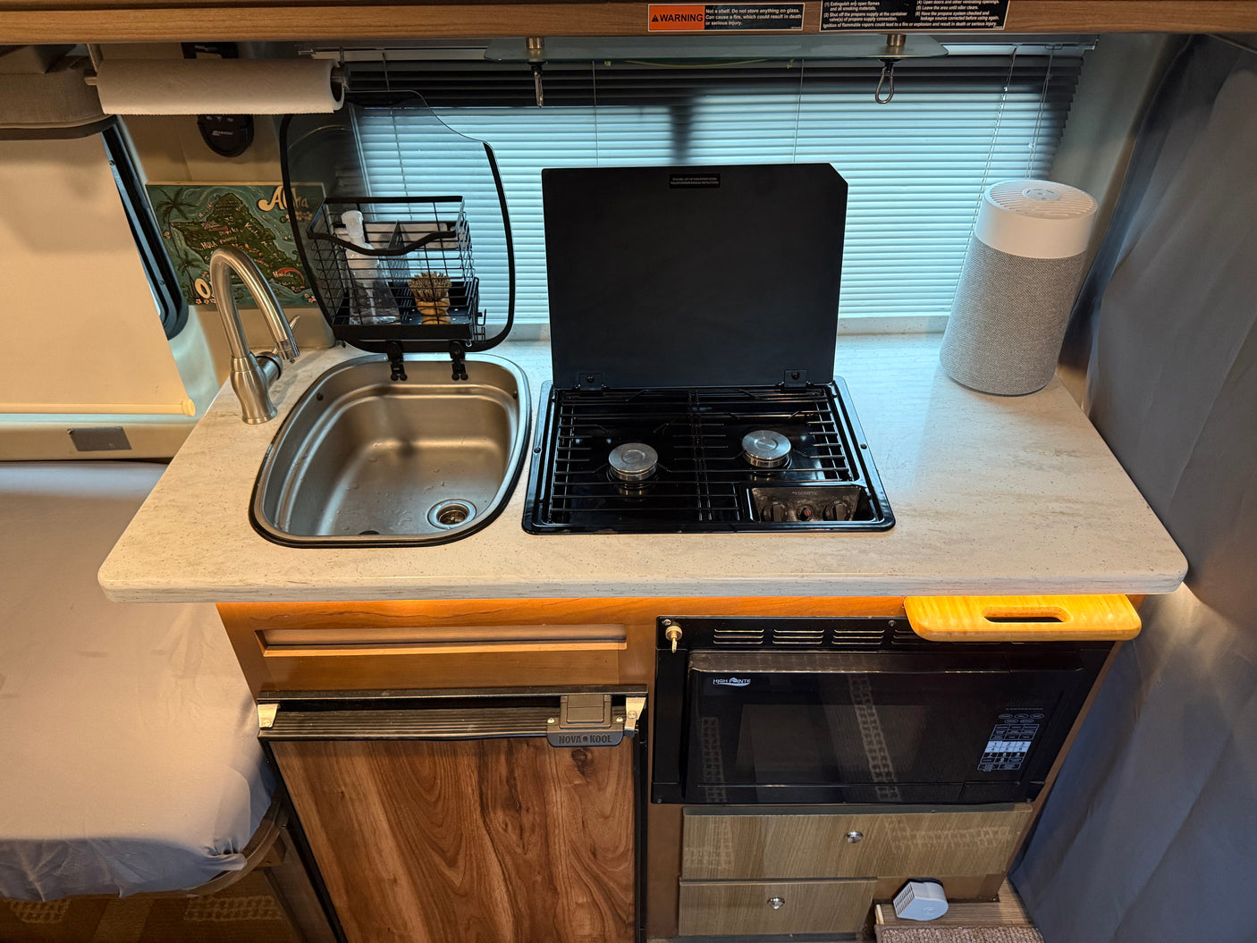 Inside an RV rental: a compact kitchen featuring a sink, two-burner stove, microwave, and refrigerator for convenient travel cooking.