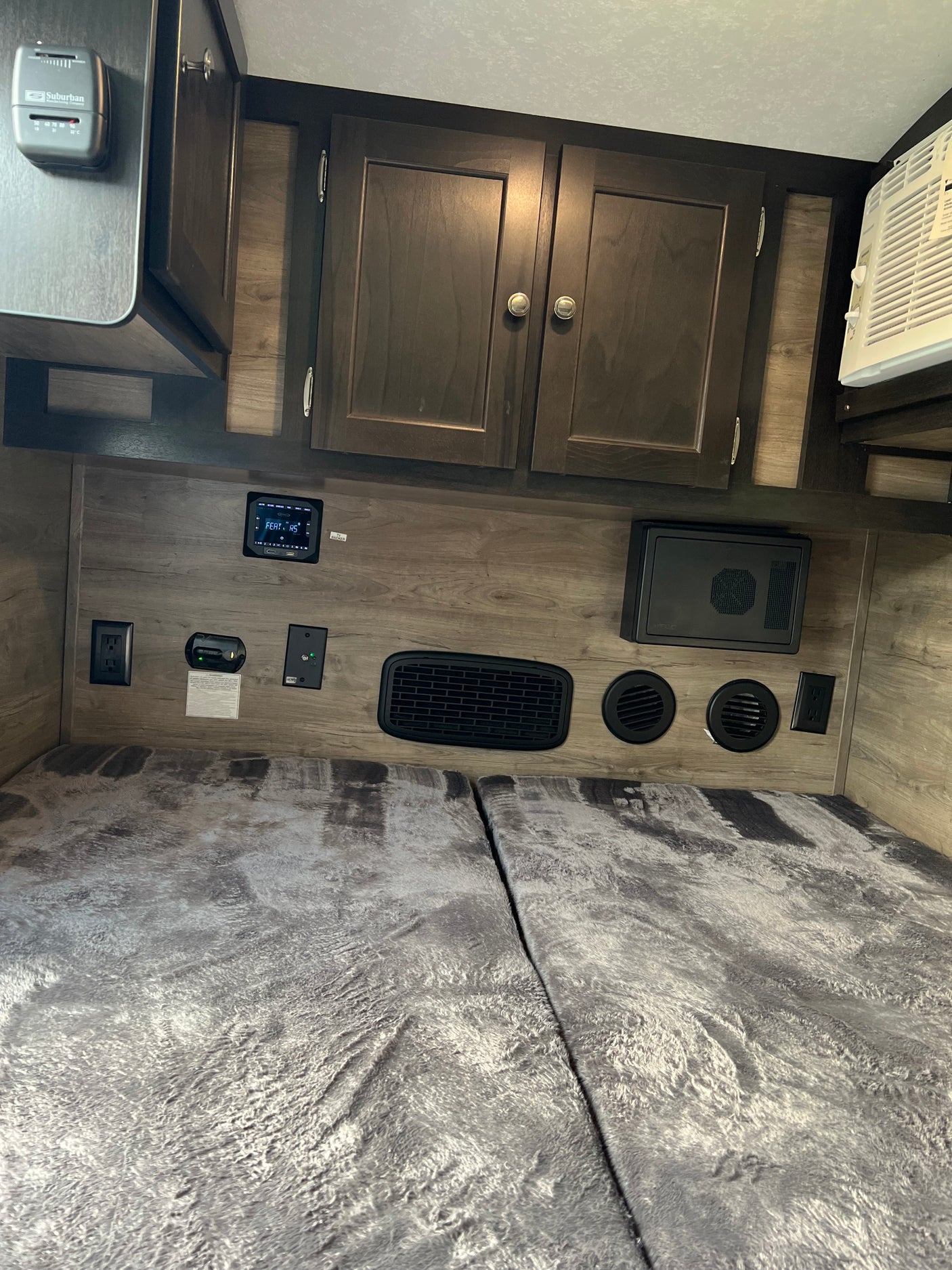 This RV rental's comfortable sleeping area includes a bed, overhead cabinets, climate control thermostat, and integrated AC unit.