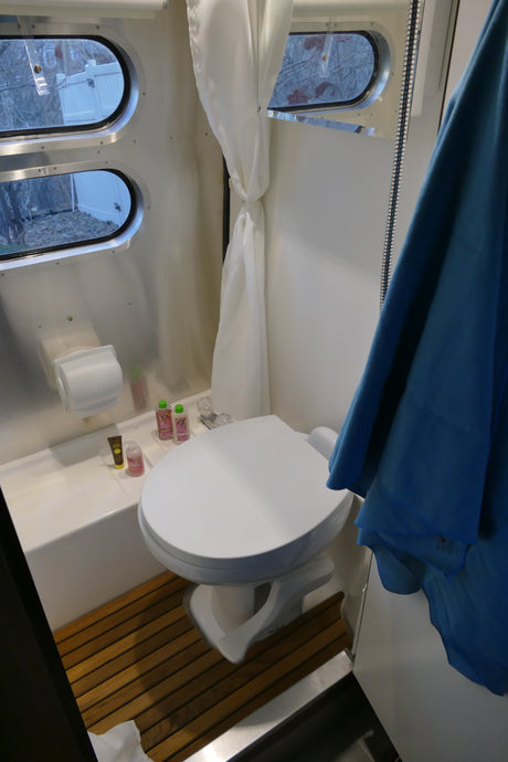 RV rental's compact bathroom features a toilet, shower, round windows, and wooden floor. Road trip ready!