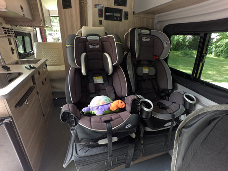 Family-friendly RV rental interior featuring two child safety seats, a kitchen, and a dinette, ready for travel with kids.