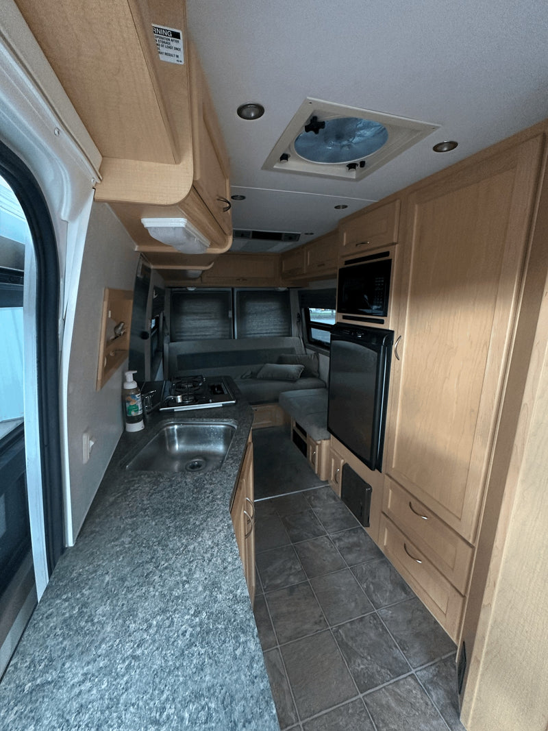 Efficient RV rental interior showcasing a compact kitchen with sink, stove, microwave, fridge, and comfortable living space. — photo 8