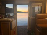 Inside an RV rental, a stunning lake sunset is visible through the open door, showing kitchen and seating areas.