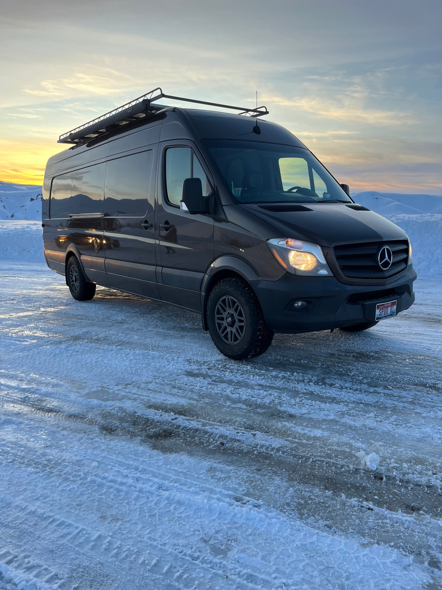 Explore snowy landscapes in this Sprinter **rv rental**. A dark van on icy ground under a vivid sunset sky.