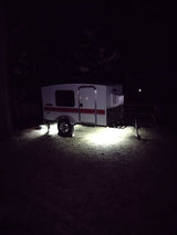 White & red compact camper RV rental, lit by underbody lights at a dark campsite. Ideal for outdoor travel.