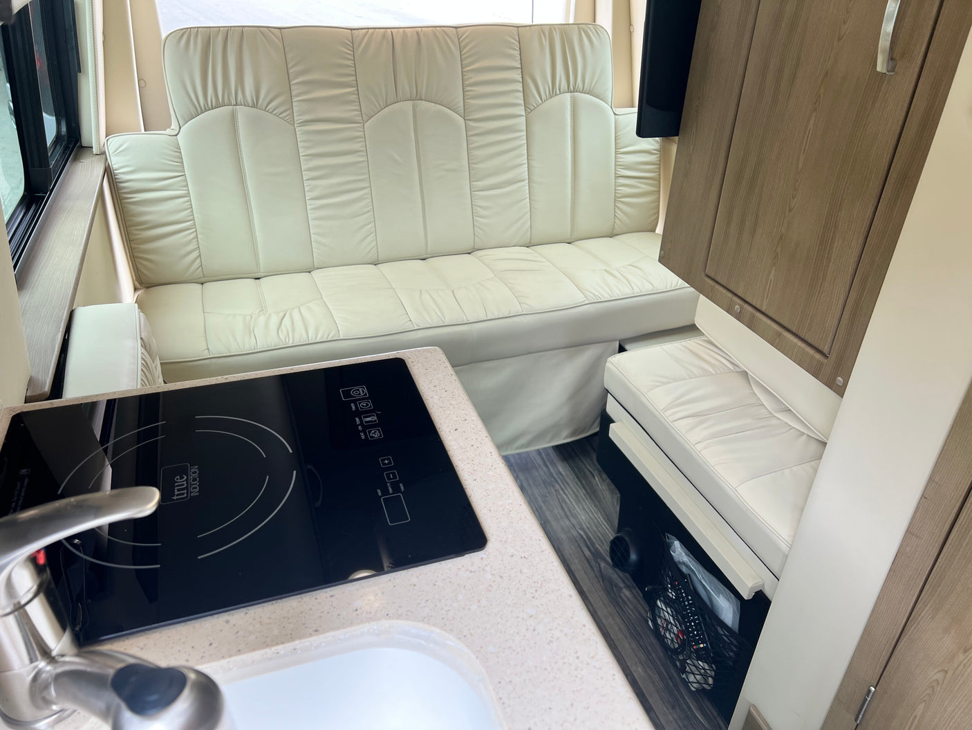 Spacious RV rental interior: cream sofa, induction cooktop, sink, and wood-look cabinets. Enjoy comfy travels!