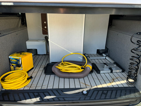 An RV rental's cargo area packed with essential camping gear: leveling blocks, water/sewer hoses, and a ladder.