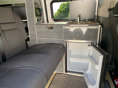 This RV rental interior features a functional kitchenette with a sink, compact fridge, and a versatile seating area.