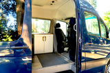 Inside view of a blue custom camper van, open door. Ideal for your next RV rental, showing a wood floor, cabinet, and front seats.