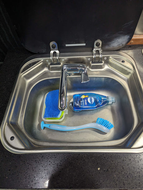 Compact RV rental kitchen sink with faucet, Dawn dish soap, sponge, and brush, ready for cleaning.