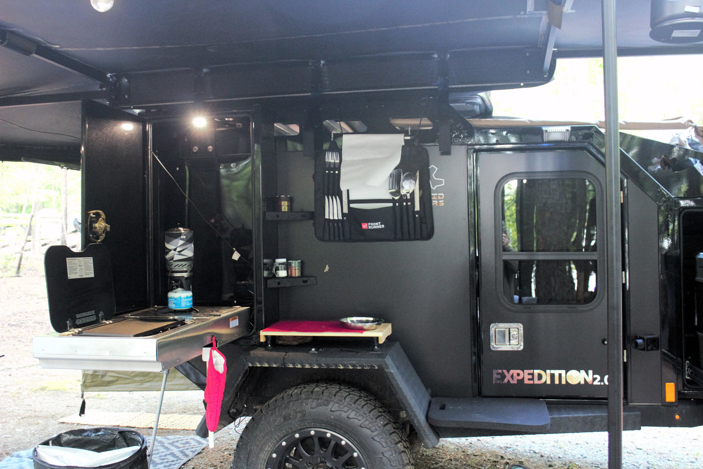 A rugged black Expedition 2.0 off-road trailer with an open side revealing an integrated outdoor kitchen, ideal for rv rental adventures.
