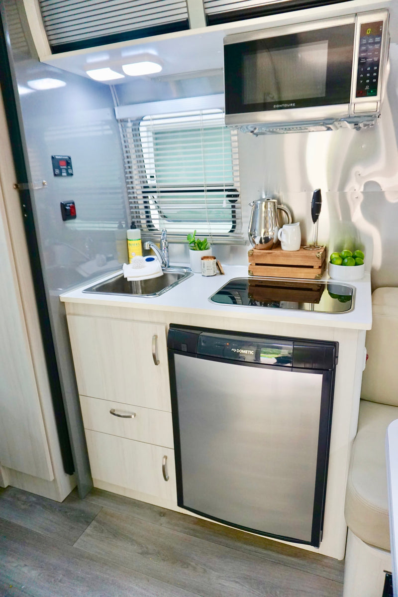 Compact rv rental kitchen: stainless steel walls, bright lights, Contoure microwave, sink, Dometic fridge, and wood floors. — photo 9