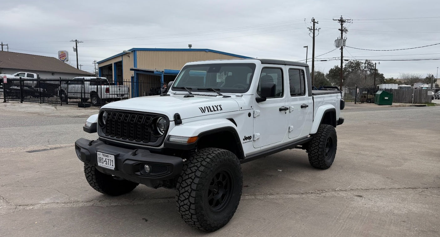 White Jeep Gladiator (Willys) pickup with large tires, parked at a service lot. Ready for adventure; consider an rv rental for longer journeys.