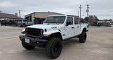 White Jeep Gladiator (Willys) pickup with large tires, parked at a service lot. Ready for adventure; consider an rv rental for longer journeys.
