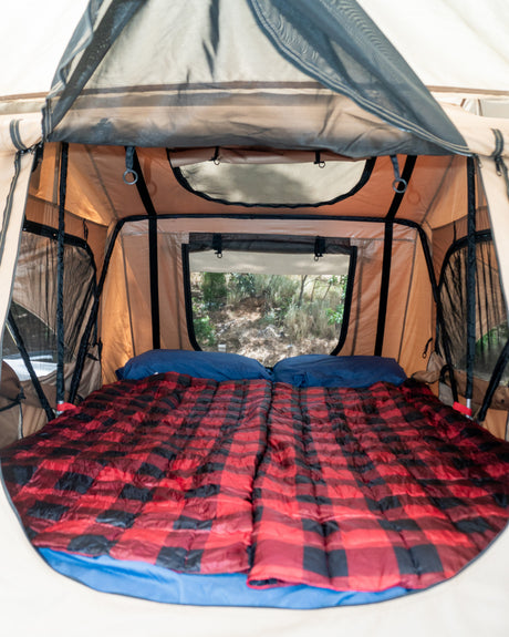 Cozy RV rental tent interior with a comfy bed, plaid bedding, and scenic window views for camping adventures.