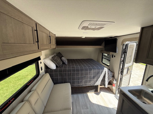 Explore this RV rental: a compact interior with a bed, sofa, kitchenette, storage, and AC unit. Ready for adventure!