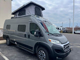 A gray Ram-based camper van with a raised pop-top roof, seen outdoors, ideal for an rv rental adventure.