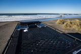 RV rental rooftop gear (solar panels, storage) overlooking a sandy beach with ocean waves, dunes, and a shipwreck.