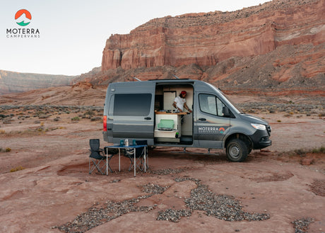Experience desert adventures with an RV rental. A grey campervan is parked in red rock landscape; person inside