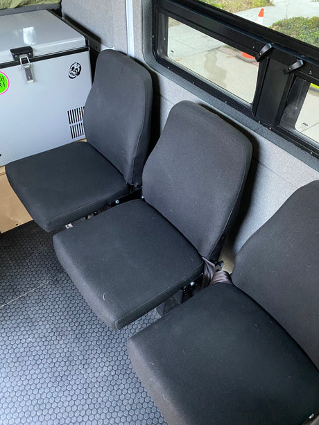 RV rental interior: three black passenger seats, a portable fridge, and textured rubber flooring, perfect for adventure.