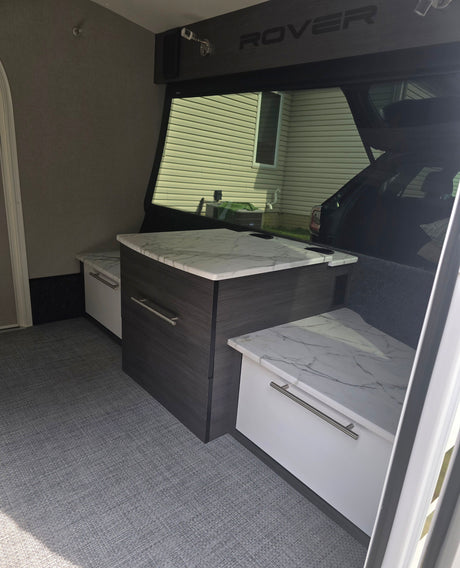 Explore this RV rental's modern interior: central dark cabinet with marble-look counter, side benches, and grey textured flooring.