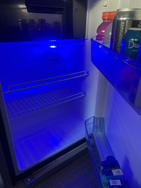 This RV rental mini-fridge, lit by a vibrant blue LED, offers compact storage for drinks and a small freezer section.