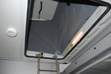 An RV rental's pop-top sleeping loft, accessed by a ladder, features a warning label & bright light.