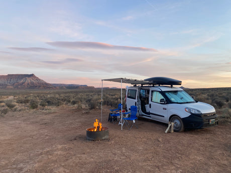 White camper van (rv rental) parked in desert. Awning, chairs, and campfire. Beautiful evening sky over distant mesas. A perfect van life adventure.