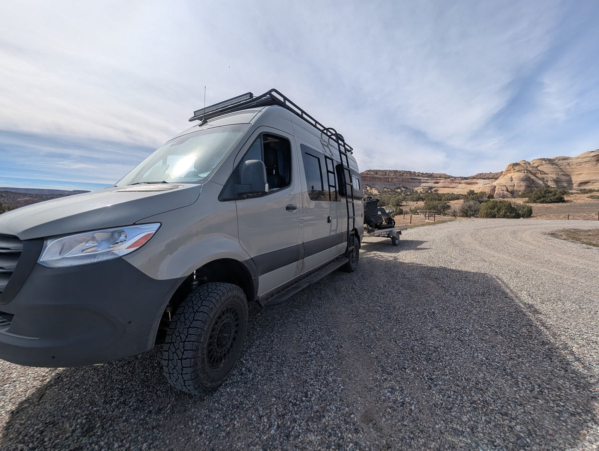 A gray Sprinter van rv rental, fully equipped for off-road adventure, towing an ATV in a scenic desert landscape. — photo 14