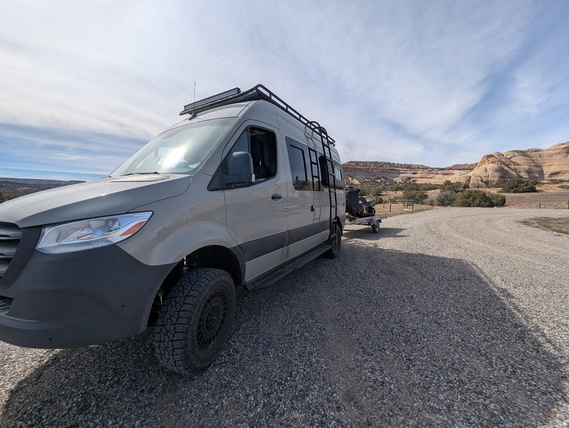 A gray Sprinter van rv rental, fully equipped for off-road adventure, towing an ATV in a scenic desert landscape. — photo 14
