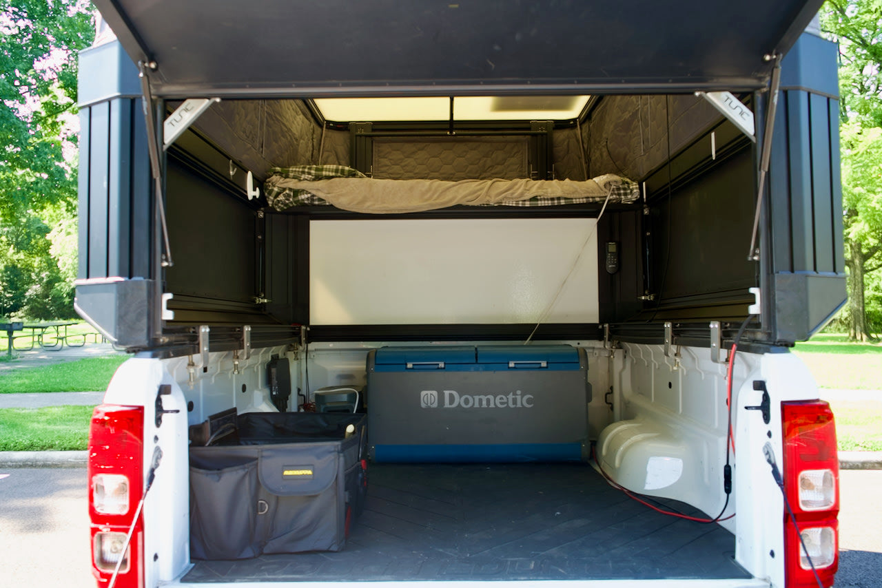 Inside a white pickup truck's open camper, showing a bed, Dometic fridge, & storage. Ideal for an RV rental camping adventure.