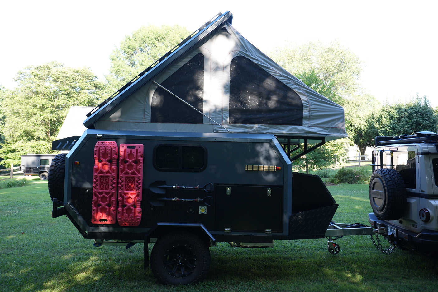 An off-road camper trailer, equipped with a pop-top tent & recovery boards, hitched to a Grenadier, ready for rv rental.