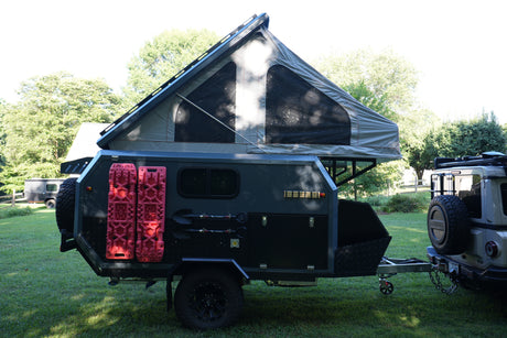 An off-road camper trailer, equipped with a pop-top tent & recovery boards, hitched to a Grenadier, ready for rv rental.