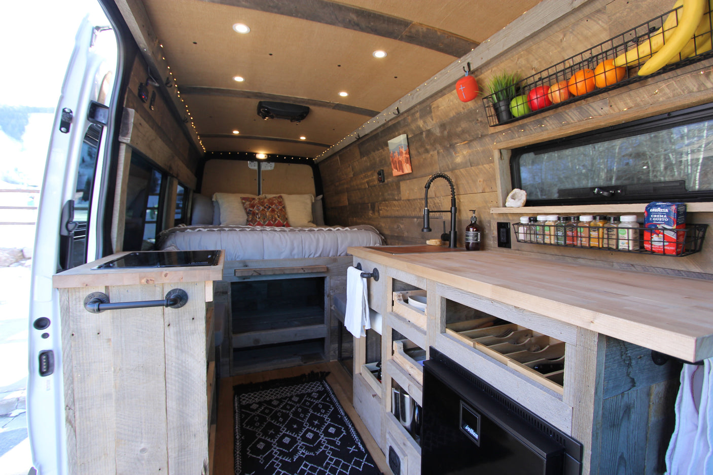This cozy RV rental camper van interior features a kitchen, bed, and rustic wood finishes, ideal for a comfortable mobile adventure.