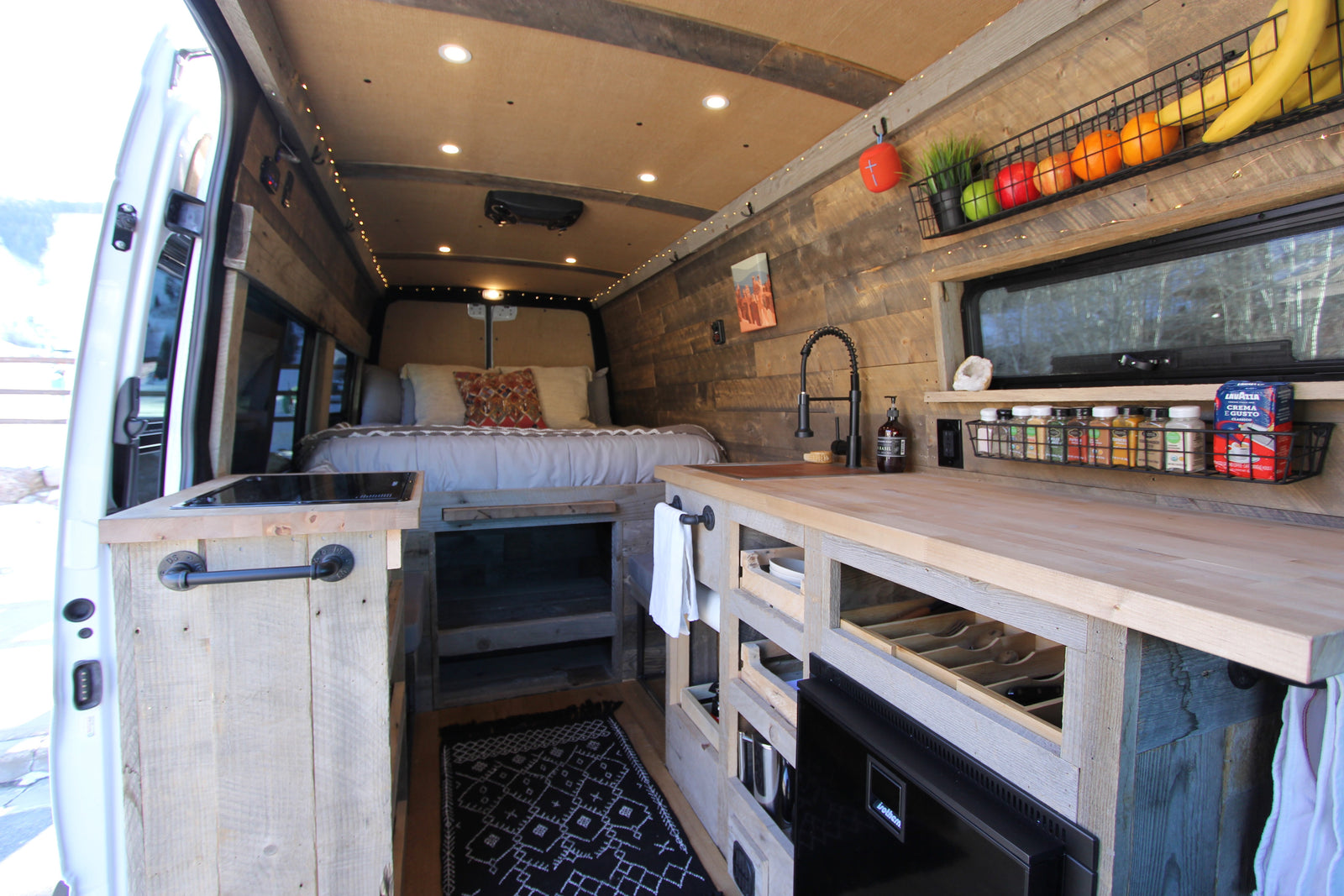 This cozy RV rental camper van interior features a kitchen, bed, and rustic wood finishes, ideal for a comfortable mobile adventure.
