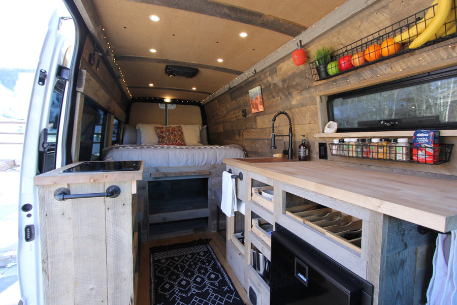 This cozy RV rental camper van interior features a kitchen, bed, and rustic wood finishes, ideal for a comfortable mobile adventure.