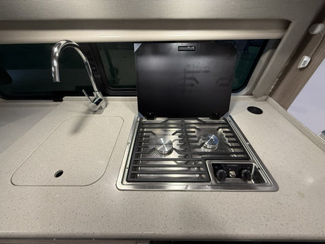 Compact RV rental kitchen featuring a shiny faucet over a sink and a Dometic two-burner stovetop with its protective lid open.