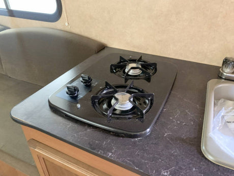 Inside an RV rental: Compact kitchen featuring a two-burner stove, sink, and dark countertop.